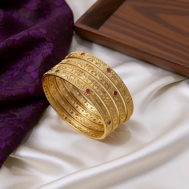 Gold bangles with red stones on a white fabric background